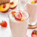 Two glasses of smoothie with a basket of peaches in the background.