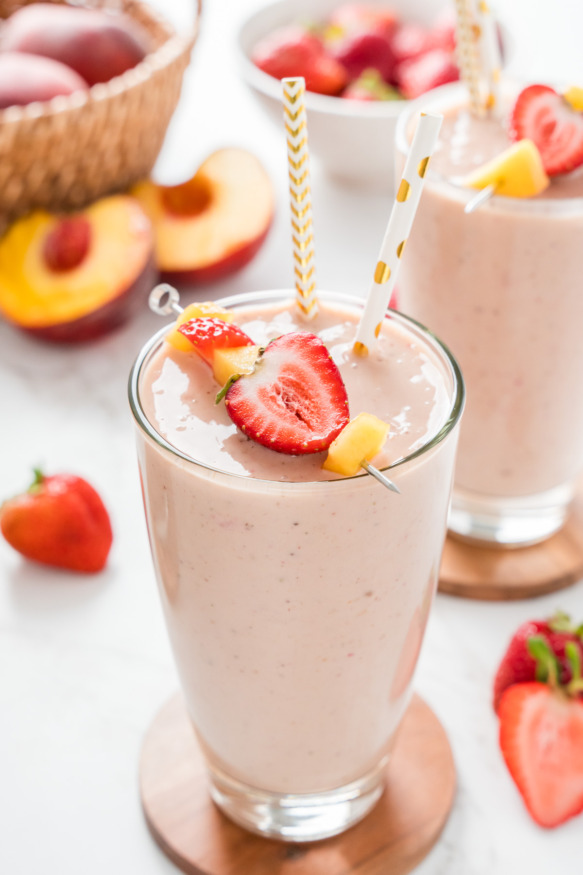 Two glasses of smoothie with a basket of peaches in the background.