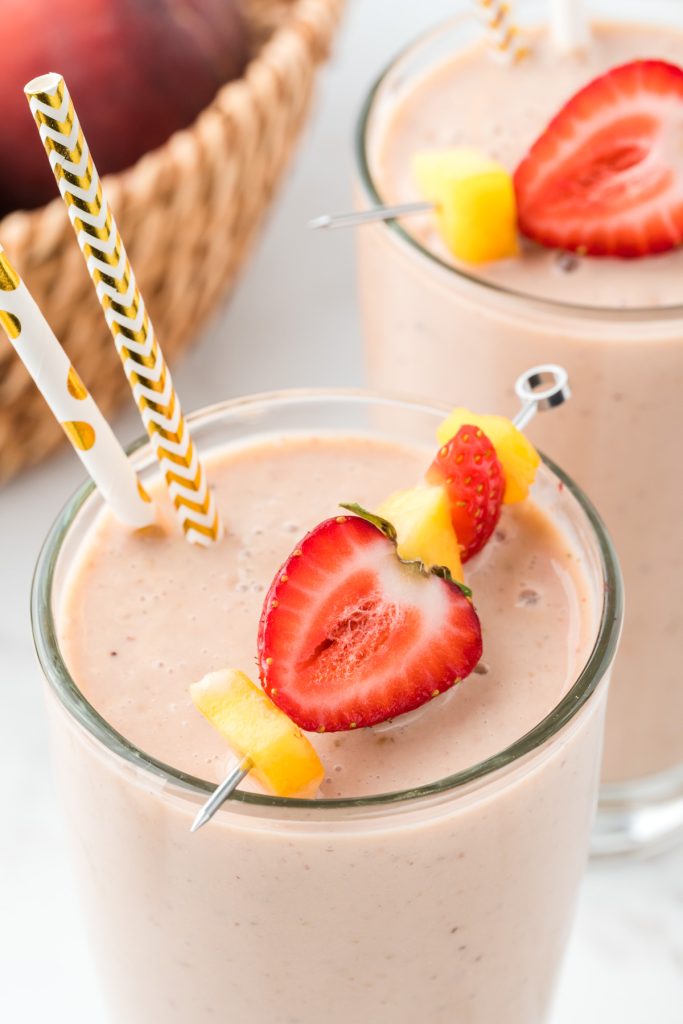 Close of up smoothie with cut fruit on top and fun paper straws.