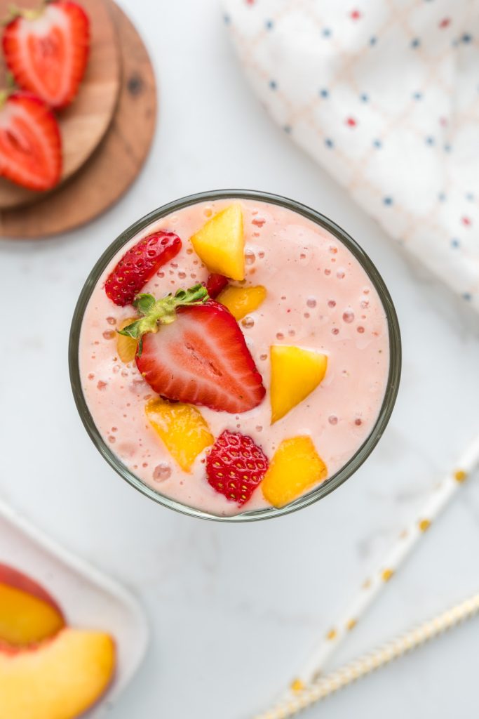 Overhead shot of smoothie in glass with cut up strawberries and peaches on top.