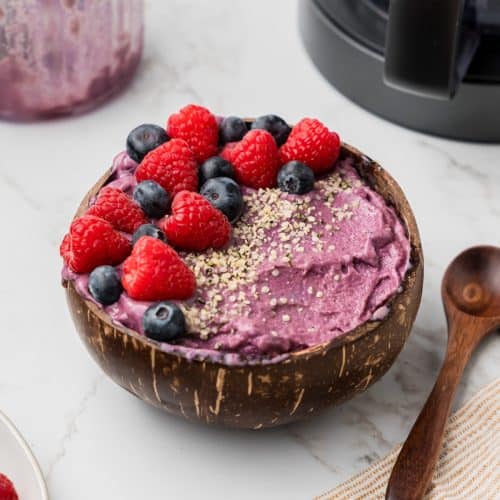 Close up of smoothie bowl with fresh fruit on top. Creami machine and empty container in the background.