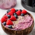 45 degree shot of smoothie bowl with fresh berries and hemp seeds on top and ninja creami and container in the background.