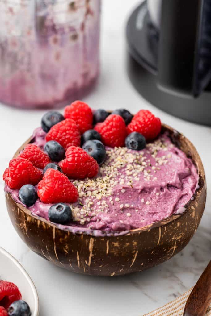 45 degree shot of smoothie bowl with fresh berries and hemp seeds on top and ninja creami and container in the background.