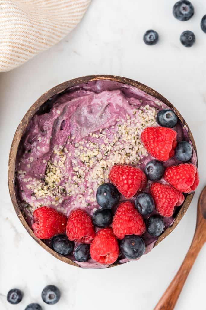 Overhead shot of purple smoothie topped with fresh berries and hemp seeds.