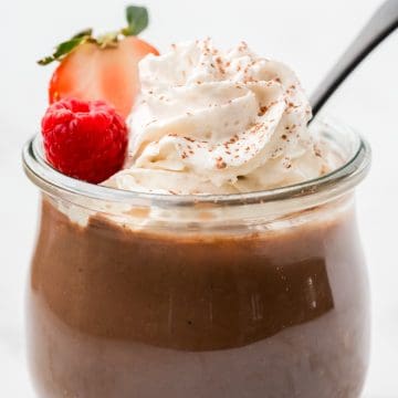 full jar of pudding topped with whipped cream and berries