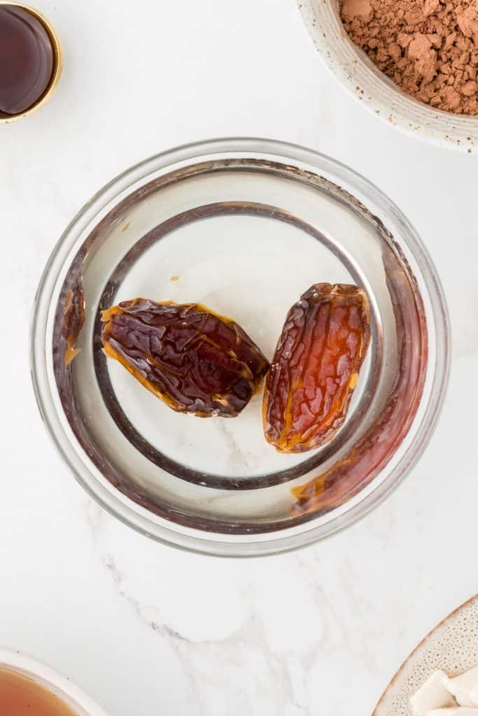 Overhead shot of two dates in a glass bowl full of water.