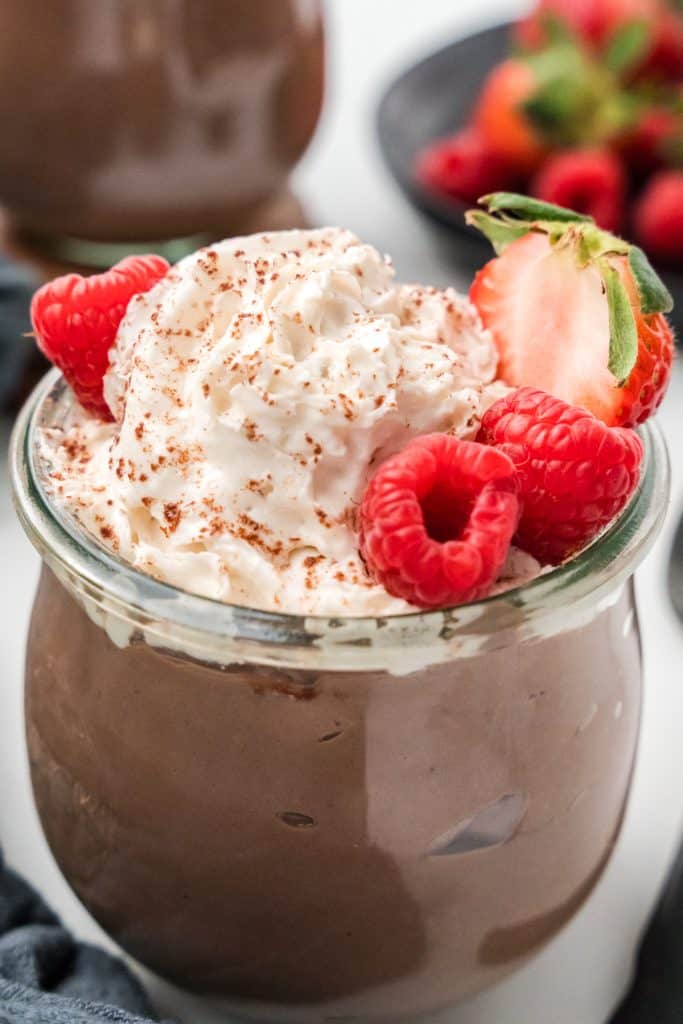 Glass jar full of pudding topped with whipped cream and raspberries and a strawberry