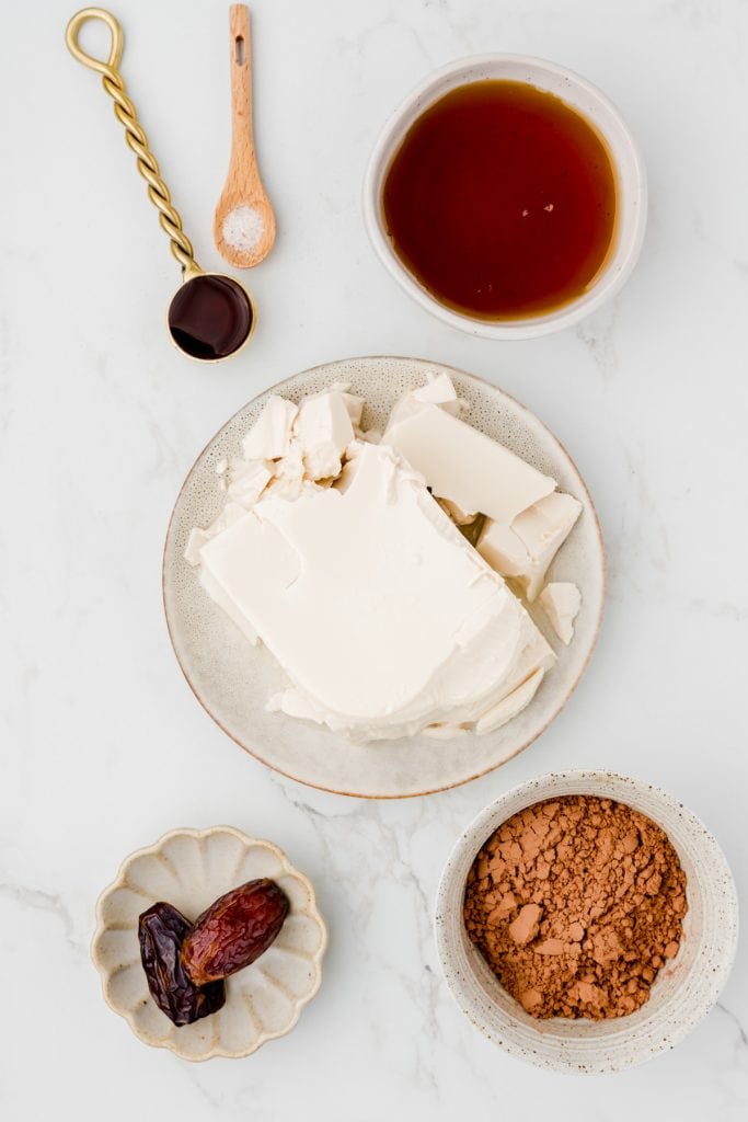 flatlay of ingredients including: silken tofu, maply syrup, cacao powder, dates, vanilla, and salt