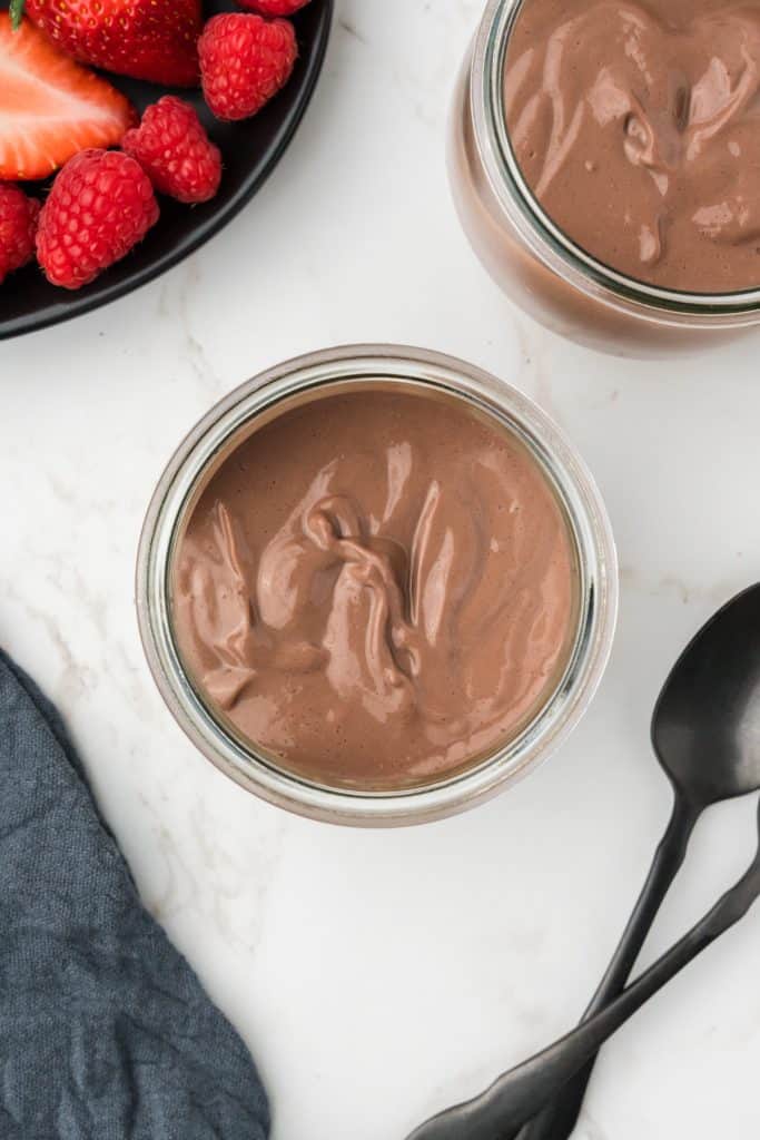 overhead shot of two glasses of pudding with spoons and berries in the corners