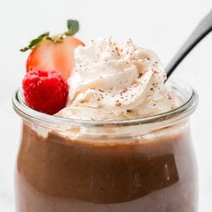 close up full jar of pudding topped with whipped cream and berries.