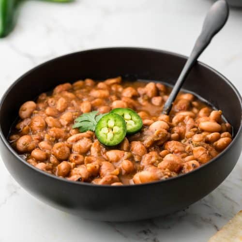 Close up of black bowl full of cooked pinto beans with a couple slices of jalapeno on top.