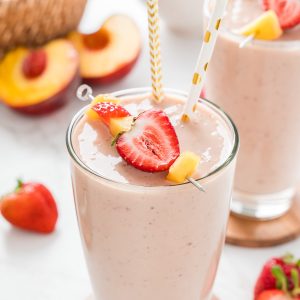 Close of up smoothie with cut fruit on top and fun paper straws.