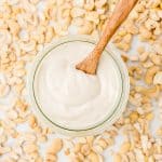 Overhead shot of mayo in a jar with a wooden spoon sitting in it. It is surrounded by cashew nuts.