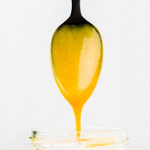 Spoon full of dressing hovering above glass jar with dressing dripping off.