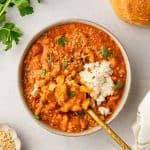 Birdseye bowl of soup in the in the middle of the image. Fresh herbs and bread in the upper corners.