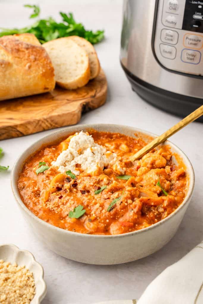 Bowl of soup in the foreground. Instant pot and a loaf of bread with a couple pieces sliced on a board in the background.