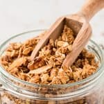 45 degree angle shot of granola in a glass jar with a wooden scoop.