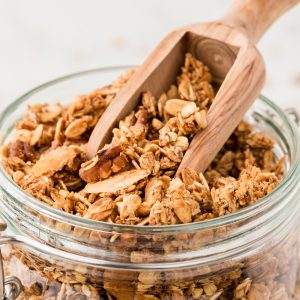45 degree angle shot of granola in a glass jar with a wooden scoop.