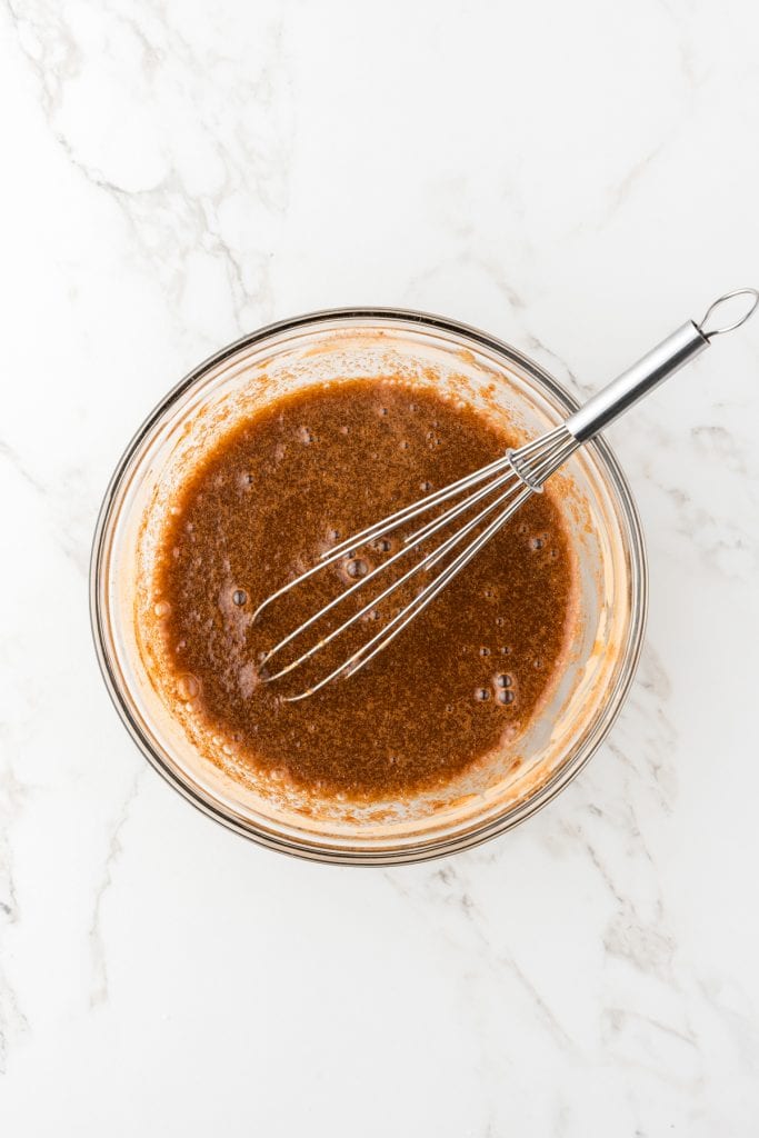 overhead shot of wet ingredients mixed together with a whisk in a glass bowl.
