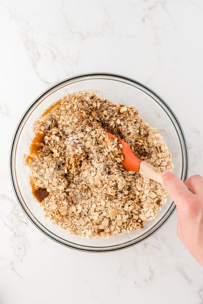 overhead shot of wet and dry ingredients being mixed together in a glass bowl with a spatula.