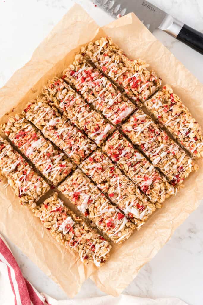 granola bars on parchment paper right after being cut, next to a knife and linen.