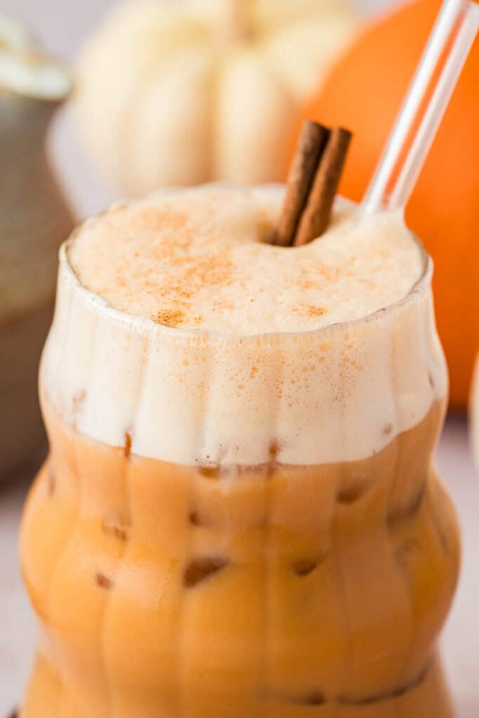 Glass full of iced pumpkin spice chai tea latte with cinnamon stick and straw.