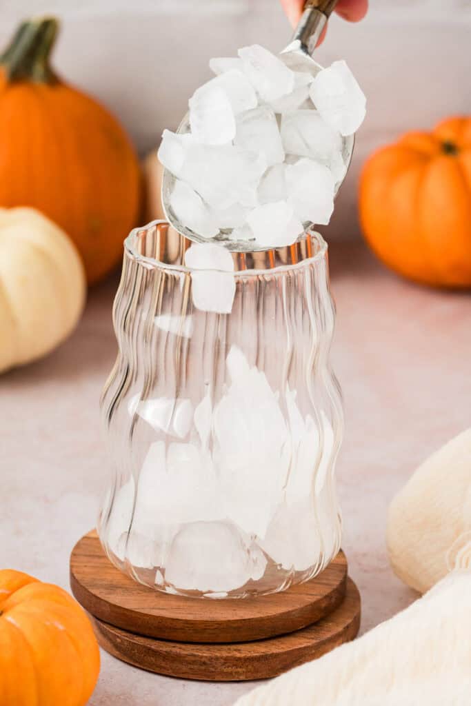 Someone pouring ice into glass cup.