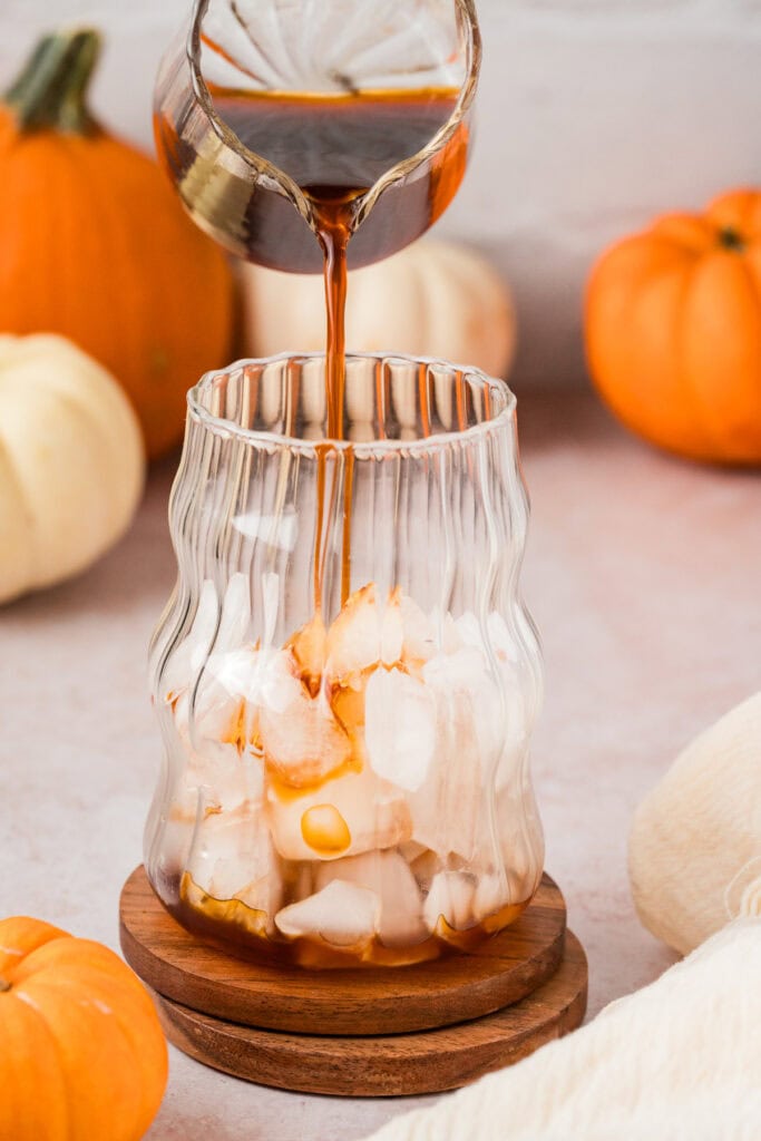 Someone pouring chai tea concentrate over ice.
