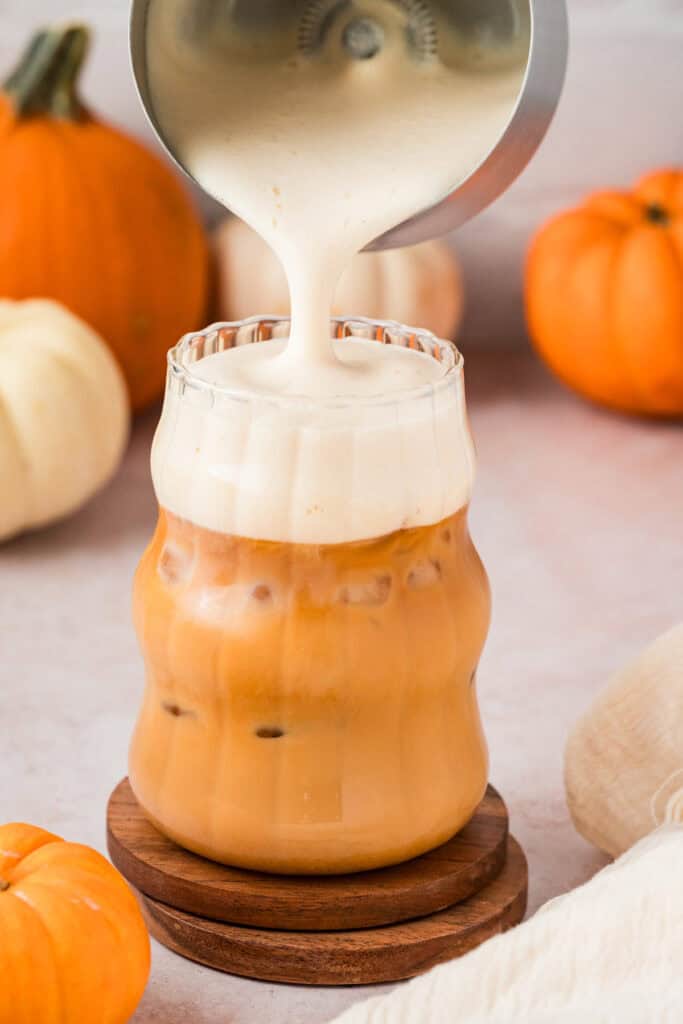Someone pouring frothed milk on top of iced chai.