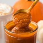 close up of a spoon spooning out some pumpkin sauce out of a glass jar.