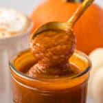 close up of a spoon spooning out some pumpkin sauce out of a glass jar.