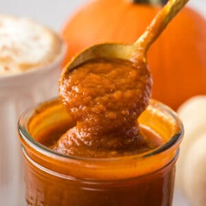 close up of a spoon spooning out some pumpkin sauce out of a glass jar.
