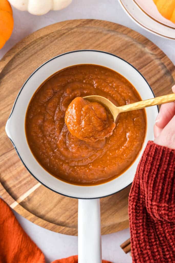 Overhead shot of completed pumpkin sauce in a white sauce pan with someone holding a spoonful overtop.