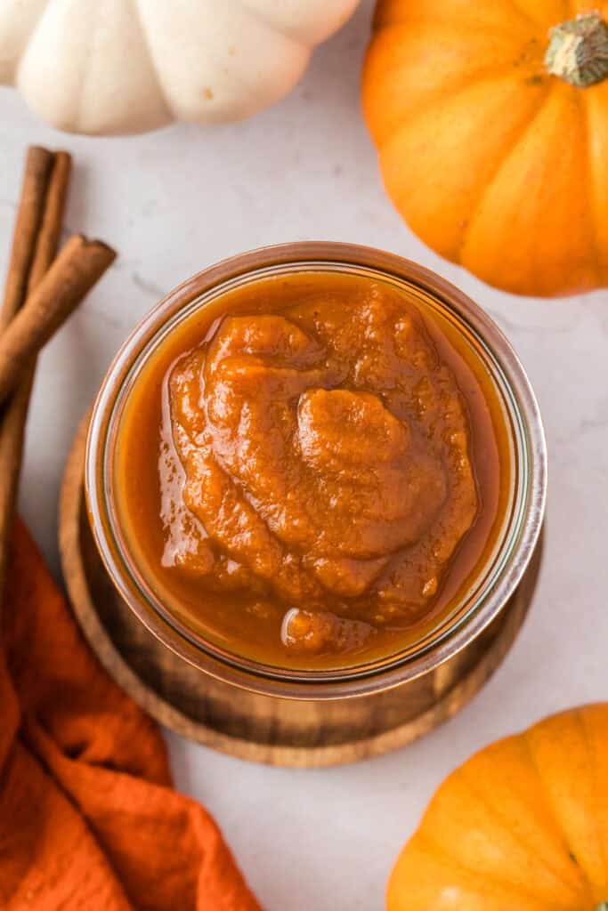 overhead shot of pumpkin sauce in a glass jar surrounded by pumpkins.