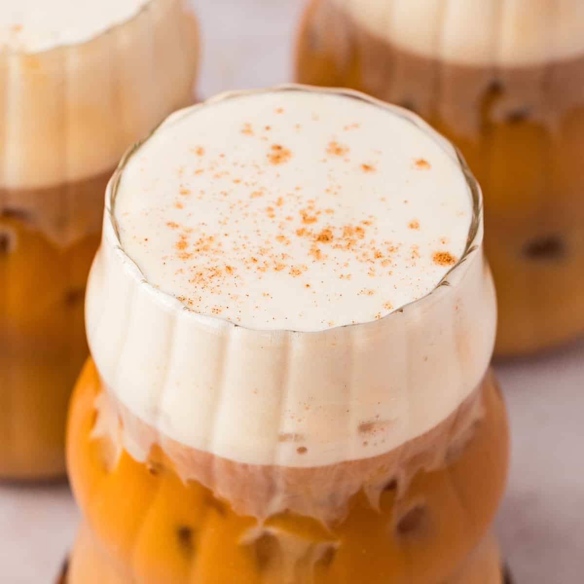 Glass full of iced pumpkin spice chai tea latte with two other glasses in the background.