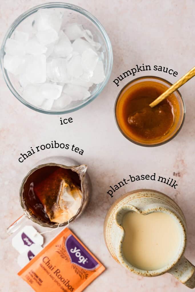 overhead shot of ingredients for iced pumpkin cream latte including: ice, pumpkin sauce, chai rooibos tea concentrated, and plant-based milk.