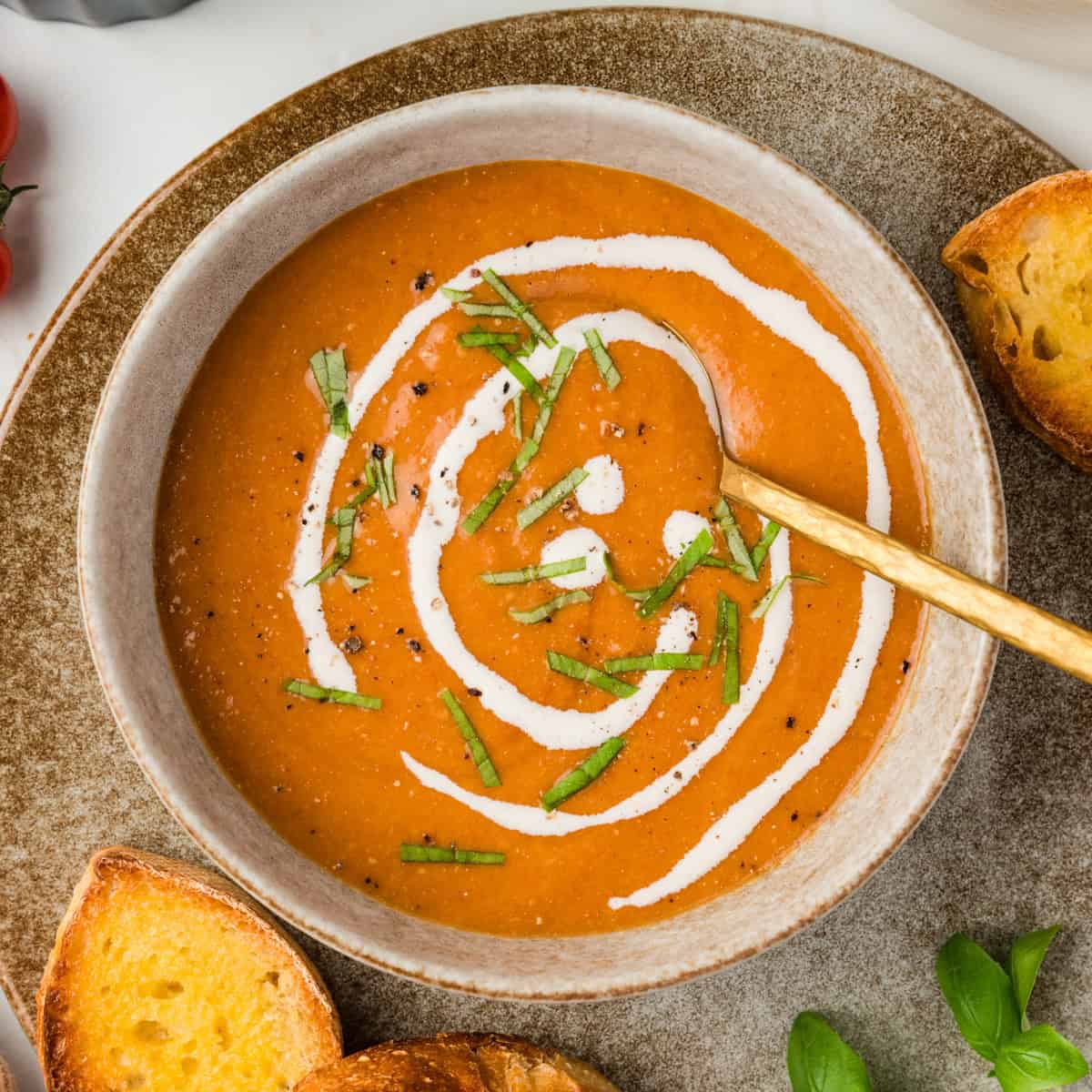 Overhead shot of tomato soup in a bowl with cream drizzled on and basil strips for garnish.